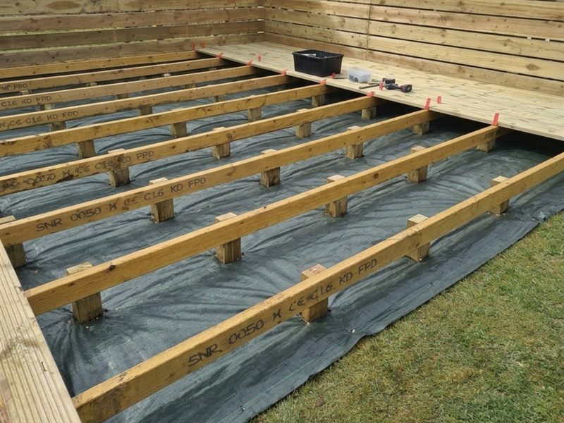 A treated timber deck frame with its supports set in concrete, built over a weed membrane, with the first boards going down