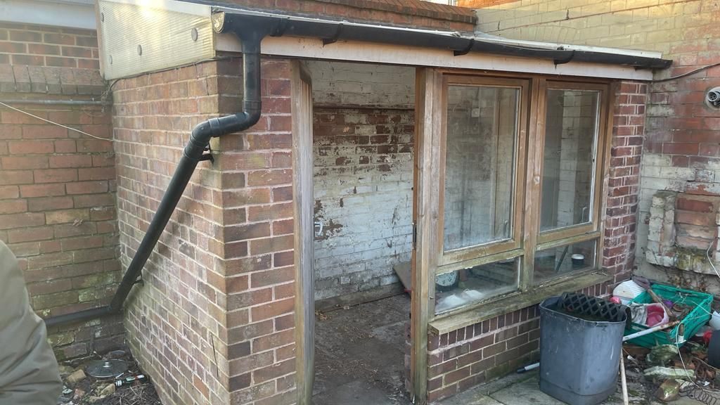 A tired brick lean-to with rotten frames and a sagging roof, before it comes down