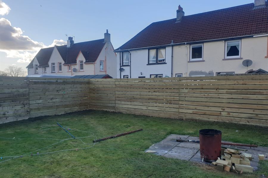 Horizontal slatted fence round a back garden with houses behind