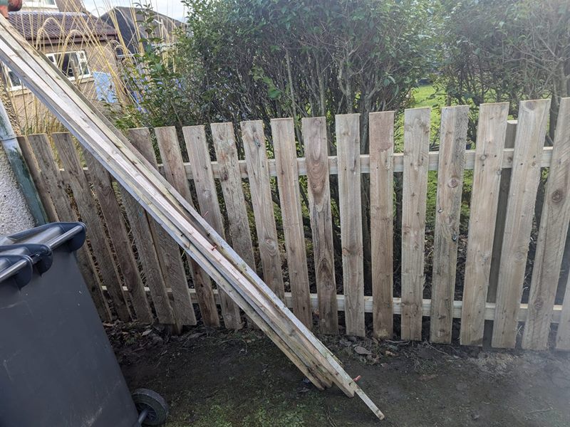 Old picket fence leaning and split, new timber stacked ready