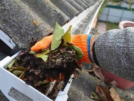 A gloved hand lifting a handful of wet leaves and silt out of a gutter