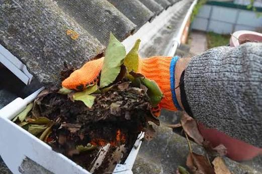 A gloved hand lifting a handful of wet leaves and silt out of a gutter