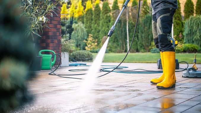 Pressure washing a paved patio, the spray lifting the dirt and the slabs running wet