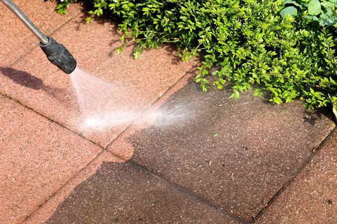 Close up of a pressure washer lance cutting a clean stripe across a dirty paving slab
