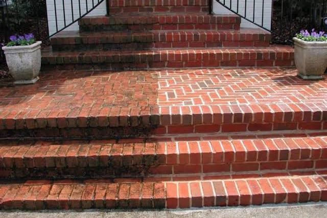 Brick steps half washed, the cleaned half bright red against the green and black of the untouched half