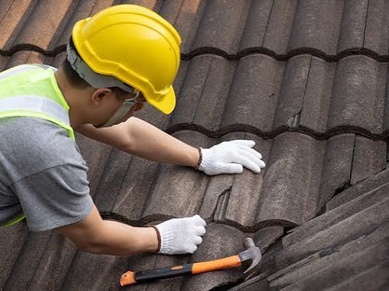 A roofer working across a tiled roof, replacing a cracked tile