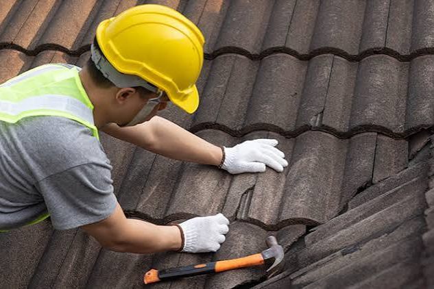 A roofer working across a tiled roof, replacing a cracked tile