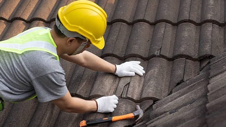 A roofer working across a tiled roof, replacing a cracked tile