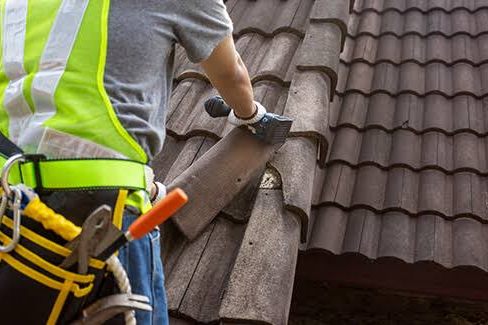 A roofer lifting a tile to get at the batten underneath
