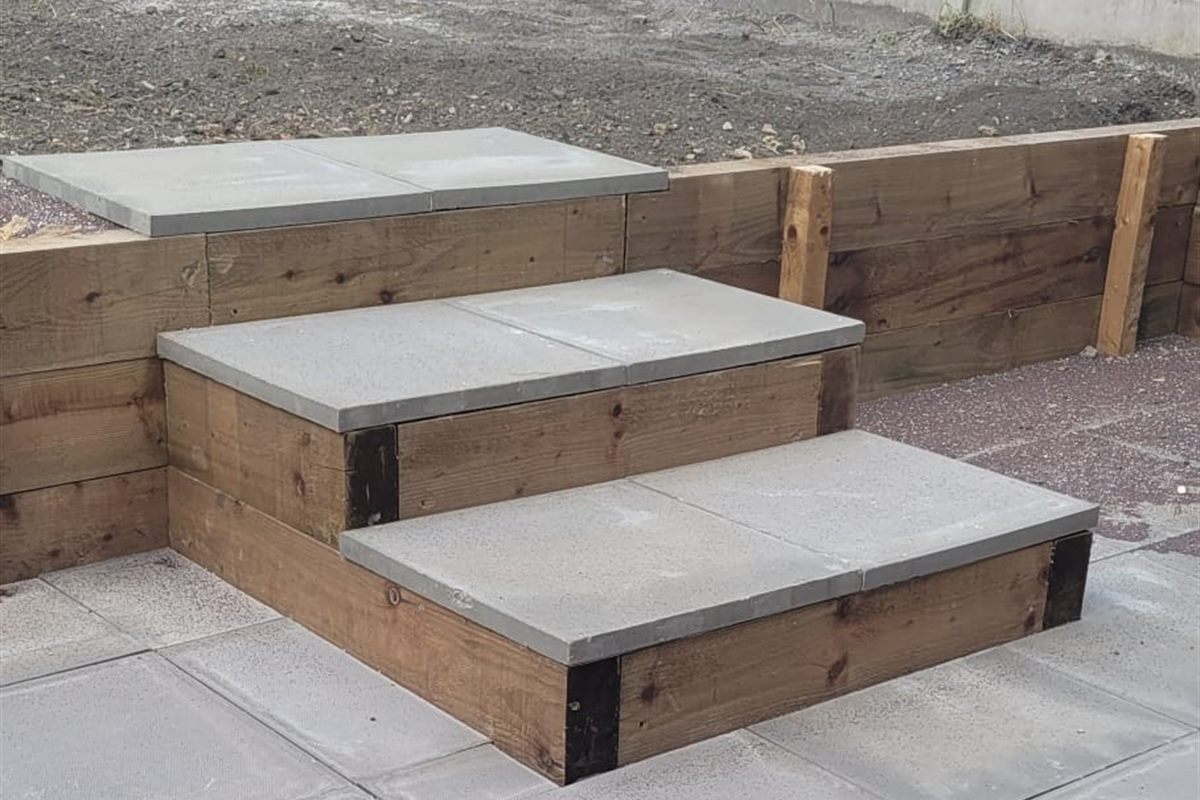 Two sleeper-and-slab steps rising from a new slabbed patio to a raised garden