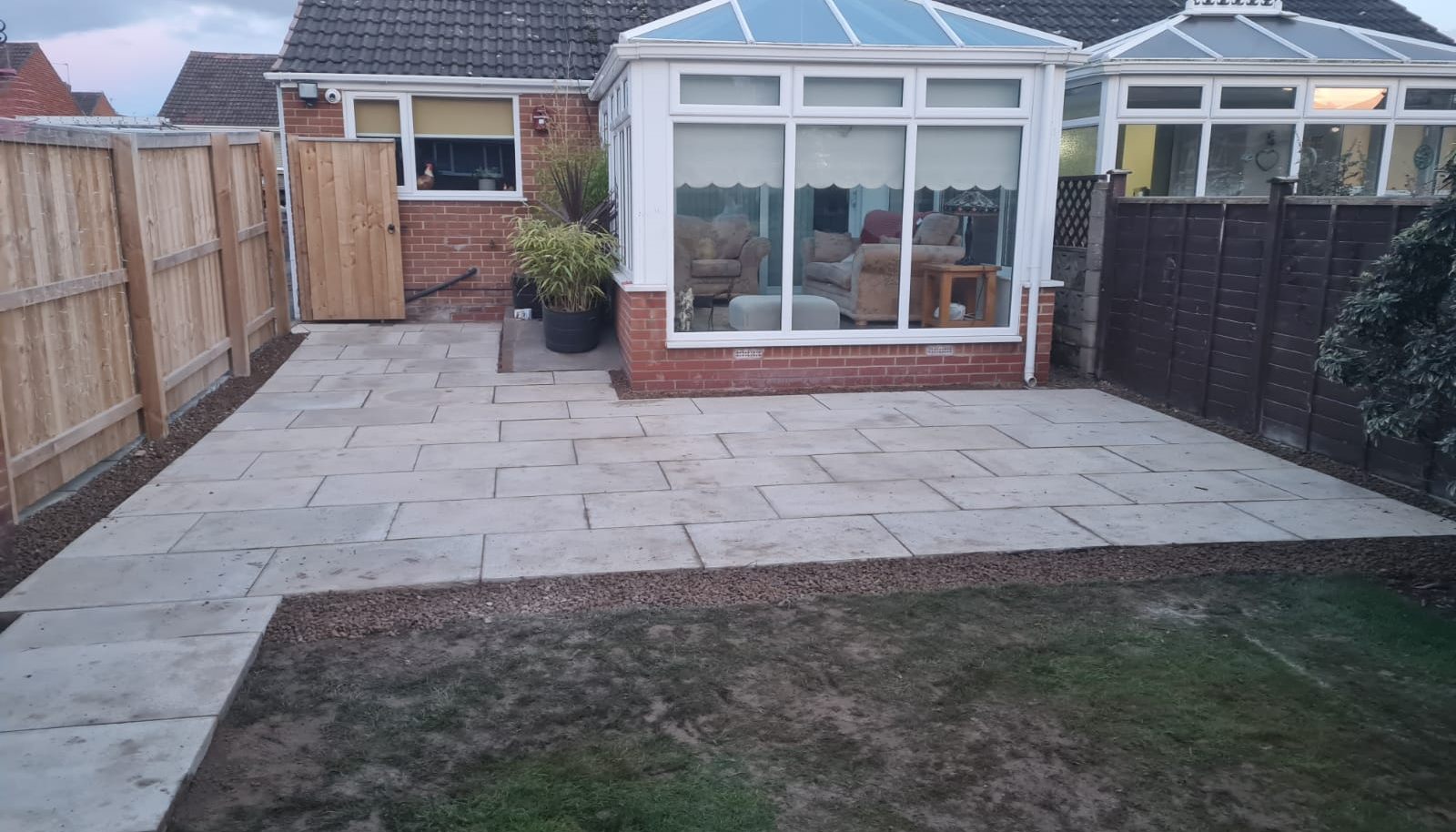 New sandstone patio laid behind a conservatory with a new fence alongside