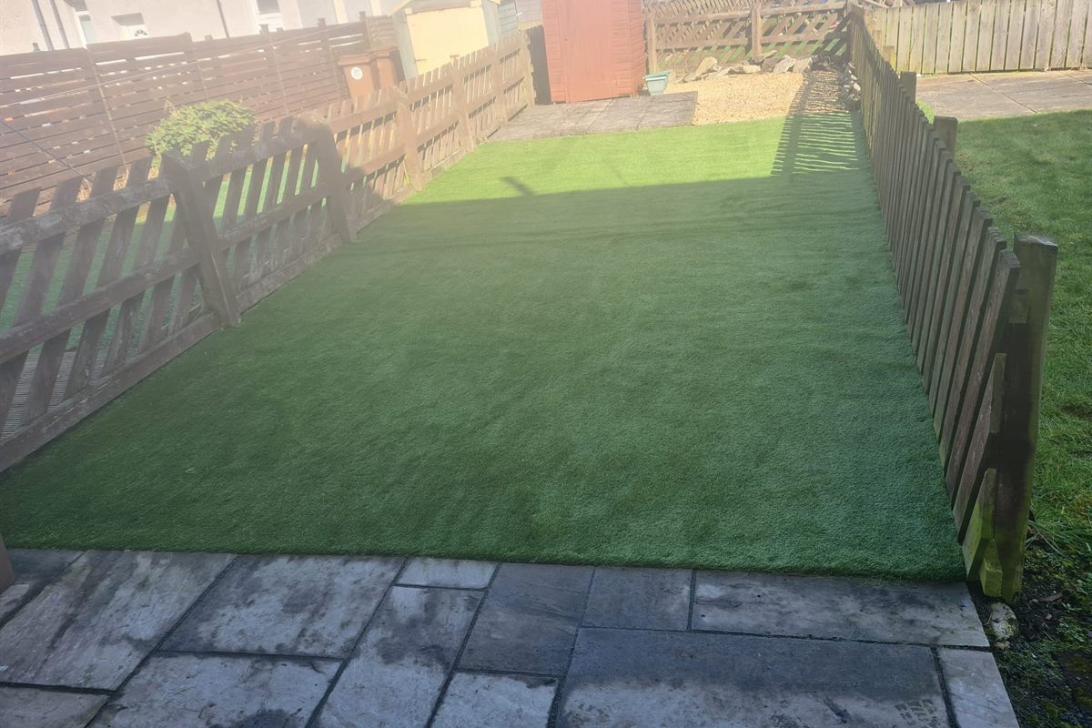 Artificial lawn laid and edged against slabs in a fenced back garden