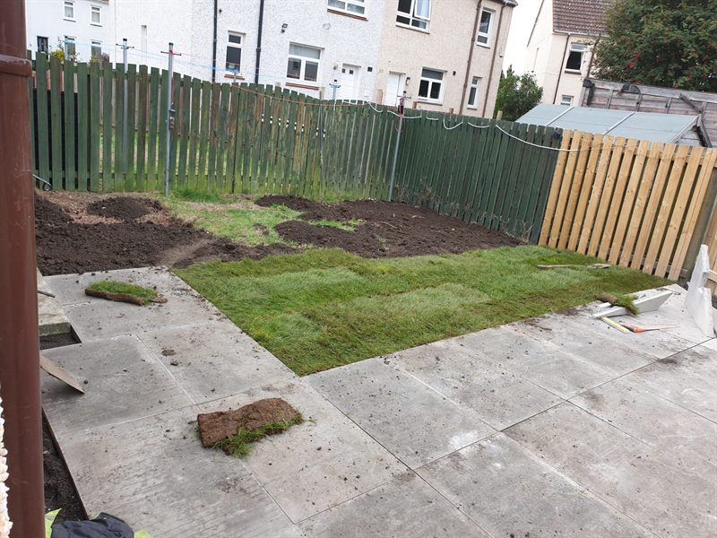 Turf rolls going down on prepared soil beside a fence