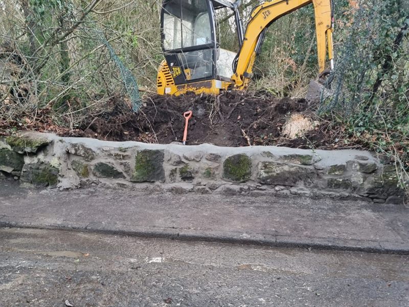 Old stone wall repointed with a mini digger clearing behind it